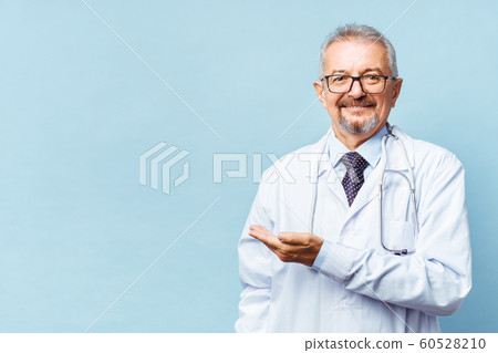 Cheerful mature doctor posing and smiling at camera, healthcare and medicine. Isolate on blue background. hand pointing at copy space. Cheerful mature doctor posing and smiling at camera, healthcare and medicine. Isolate on blue background. hand pointing at copy space. 60528210