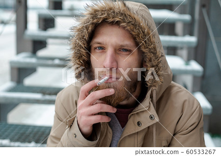 A bearded young man smokes a cigarette in winter A bearded young man smokes a cigarette in winter 60533267