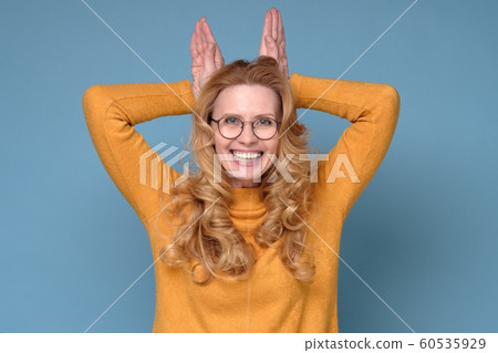 Mature woman with curly hair standing with funny face and bunny ears gesture 60535929