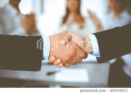 Business people shaking hands at meeting while theirs colleagues clapping and applauding. Group of unknown businessmen and women in modern white office. Success teamwork, partnership and handshake Business people shaking hands at meeting while theirs colleagues clapping and applauding. Group of unknown businessmen and women in modern white office. Success teamwork, partnership and handshake 60543021