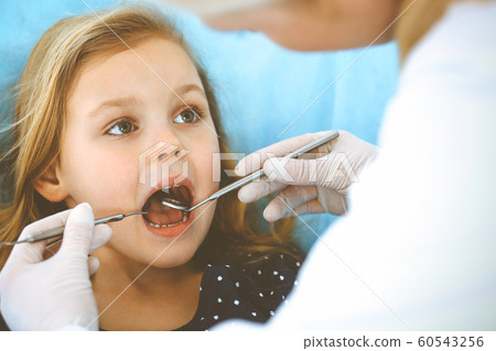 Little baby girl sitting at dental chair with open mouth during oral check up while doctor. Visiting dentist office. Medicine concept. Toned photo Little baby girl sitting at dental chair with open mouth during oral check up while doctor. Visiting dentist office. Medicine concept. Toned photo 60543256