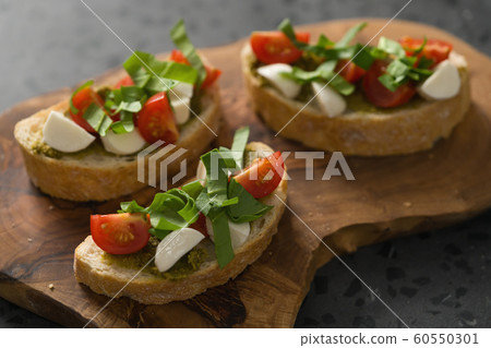 Bruschetta with mozzarella, cherry tomatoes and pesto on olive board 60550301