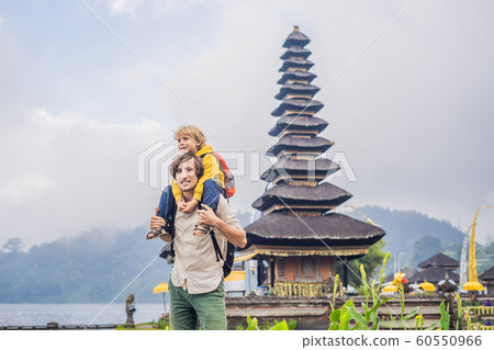 Dad and son in the background of Pura Ulun Danu Bratan, Bali. Hindu temple surrounded by flowers on Bratan lake, Bali. Major Shivaite water temple in Bali, Indonesia. Hindu temple. Traveling with Dad and son in the background of Pura Ulun Danu Bratan, Bali. Hindu temple surrounded by flowers on Bratan lake, Bali. Major Shivaite water temple in Bali, Indonesia. Hindu temple. Traveling with 60550966