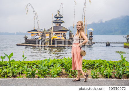 Young woman traveler in the background of Pura Ulun Danu Bratan, Bali. Hindu temple surrounded by flowers on Bratan lake, Bali. Major Shivaite water temple in Bali, Indonesia. Hindu temple 60550972