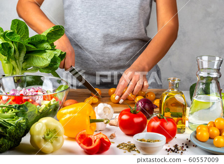Woman cuts yellow cherry tomatoes and cooking salad in the kitchen. Healthy diet concept. Woman cuts yellow cherry tomatoes and cooking salad in the kitchen. Healthy diet concept. 60557009