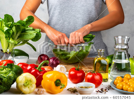 Woman is preparing green salad of romaine lettuce, cooking salad in a glass bowl in the kitchen. Healthy diet concept. 60557045