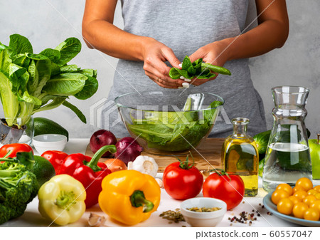 Woman is preparing green salad of romaine lettuce, cooking salad in a glass bowl in the kitchen. Healthy diet concept. 60557047