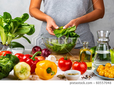 Woman is preparing green salad of romaine lettuce, cooking salad in a glass bowl in the kitchen. Healthy diet concept. 60557048