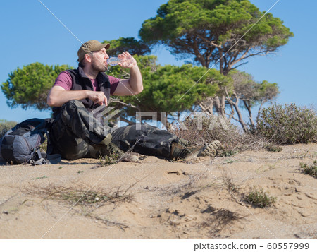 Tourist man drinking water from the plastic bottle during break in a desert walk. 60557999