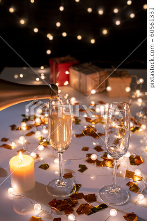 Two flutes and burning candle on table among golden confetti and lit garlands 60561331