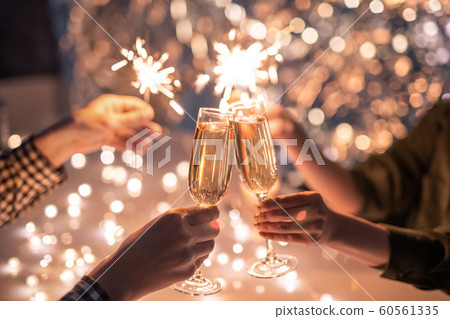 Hands of couple with flutes of champagne and their friends with bengal lights 60561335