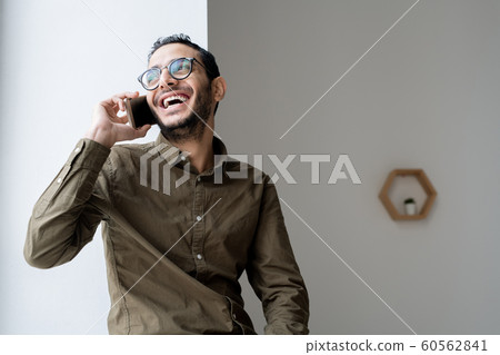 Happy young casual businessman talking on mobile phone by office window 60562841