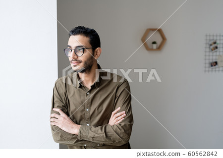 Young cross-armed businessman in eyeglasses and shirt looking through window 60562842