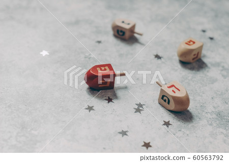 Hanukkah holiday concept. Closeup of wooden dreidel toys, golden and silver confetti stars decoration on grunge concrete background. Jewish holiday design. Empty copy space, selective focus. Hanukkah holiday concept. Closeup of wooden dreidel toys, golden and silver confetti stars decoration on grunge concrete background. Jewish holiday design. Empty copy space, selective focus. 60563792