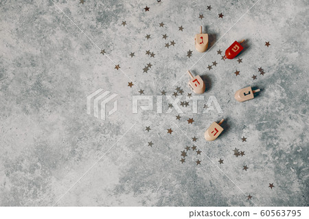 Hanukkah styled stock composition. Decorative pattern. Wooden dreidel toys, golden and silver confetti stars decoration on grunge concrete background. Flat lay, top view. Jewish holiday design. Hanukkah styled stock composition. Decorative pattern. Wooden dreidel toys, golden and silver confetti stars decoration on grunge concrete background. Flat lay, top view. Jewish holiday design. 60563795