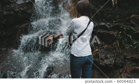 woman reaching out hands to splashing waterfall 60564823