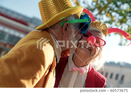 Aged man in clown costume kissing wife outdoors stock photo Aged man in clown costume kissing wife outdoors stock photo 60573675