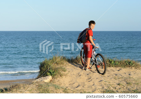 a boy with a Bicycle on a hill looks at the sea 60575660
