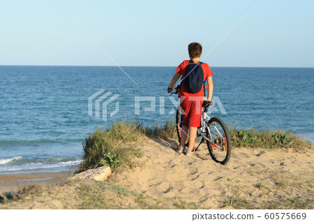 a boy with a Bicycle on a hill looks at the sea 60575669