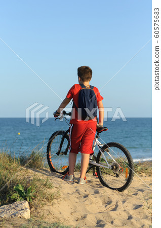 a boy with a Bicycle on a hill looks at the sea a boy with a Bicycle on a hill looks at the sea 60575683