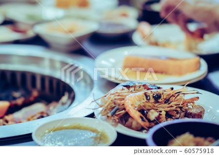 People grilling meat on a smokeless barbecue grill in a restaurant. Selective focus on shrimps. 60575918