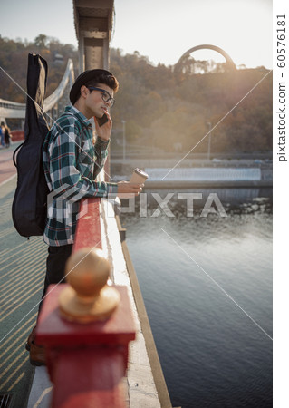 Young guy in hat and glasses staying with guitar Young guy in hat and glasses staying with guitar 60576181