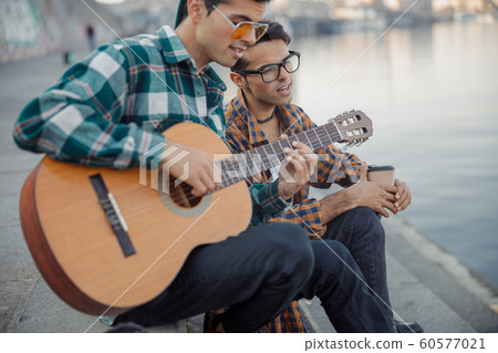 Male twins sitting near the river with a guitar Male twins sitting near the river with a guitar 60577021