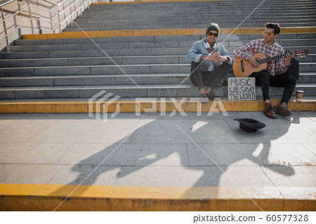 Stylish young guy sitting with hot drink near his friend Stylish young guy sitting with hot drink near his friend 60577328