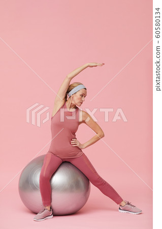 Active Mature Woman Stretching against Pink 60580134