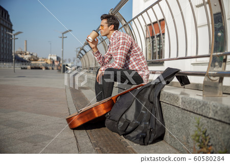 Young guy sitting outdoors with his instrument Young guy sitting outdoors with his instrument 60580284