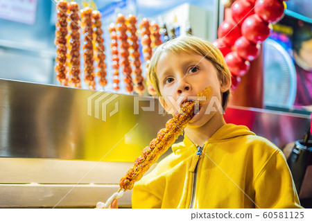 Boy eating Traditional Chinese Dessert - Candied Fruit on a Wooden Stick 60581125