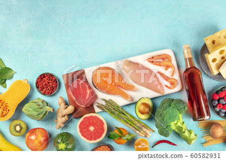Food, a flat lay of many different products, with meat, fish, chicken and shrimps, vegetables and fruits, wine and cheese, shot from the top on a blue background with a place for text 60582931