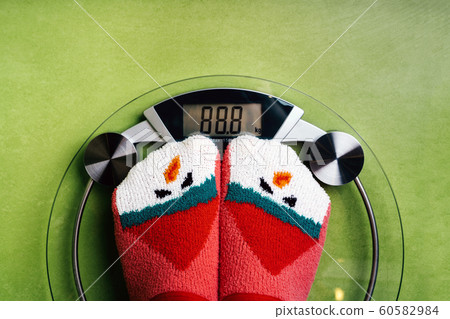 Girl standing on the scales in Christmas fun red green socks with snowman Girl standing on the scales in Christmas fun red green socks with snowman 60582984
