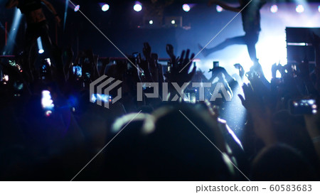 Big crowd dancing with their hands up at the rock concert - blue lighting Big crowd dancing with their hands up at the rock concert - blue lighting 60583683