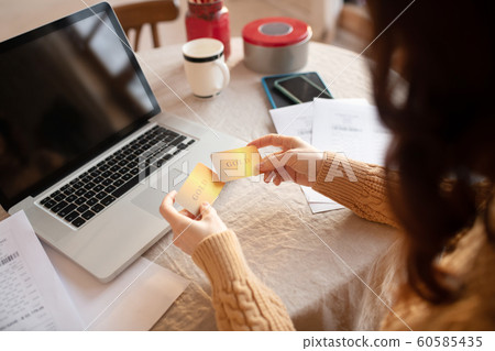 Long-haired young woman in sweater holding a credit card Long-haired young woman in sweater holding a credit card 60585435