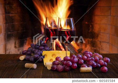 Two glasses of red wine with cheese and grapes near the fireplace. Two glasses of red wine with cheese and grapes near the fireplace. 60585584