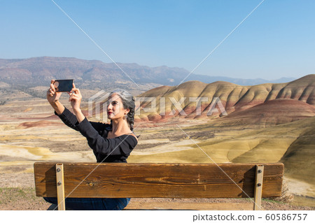 A young brunette with gray strands makes selfies sitting on a bench in Painted Hills Overlook 60586757