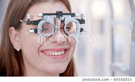 Ophthalmology - a young smiling woman with a device for vision test on her nose Ophthalmology - a young smiling woman with a device for vision test on her nose 60588853