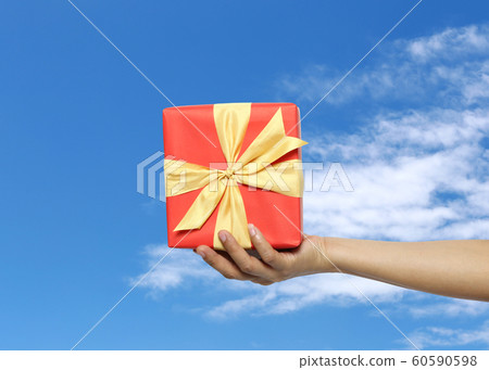 Women's hand holding a red gift box on Blue sky background. Women's hand holding a red gift box on Blue sky background. 60590598