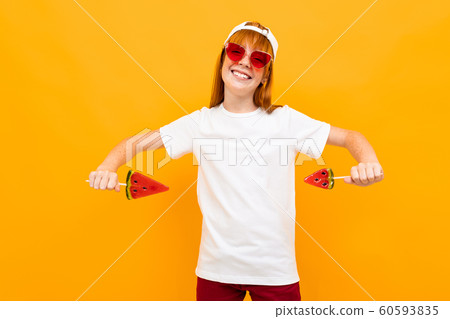 smiling european red-haired girl in a white t-shirt and sunglasses with candy in hand on a yellow 60593835