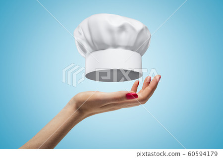 Side closeup of woman's hand facing up and levitating toque blanche on light blue gradient background. Side closeup of woman's hand facing up and levitating toque blanche on light blue gradient background. 60594179