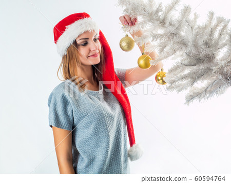 Young woman in Santa hat hanging ball on a Christmas tree Young woman in Santa hat hanging ball on a Christmas tree 60594764