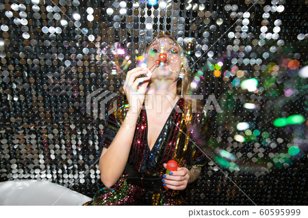 Young glamorous woman in glittering dress blowing soap bubbles at party 60595999