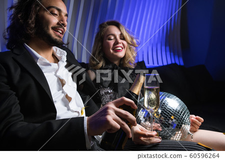 Happy young man with bottle of champagne going to pour wine into flute Happy young man with bottle of champagne going to pour wine into flute 60596264