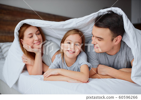 portrait of smiling parents and daughter on bed 60596266