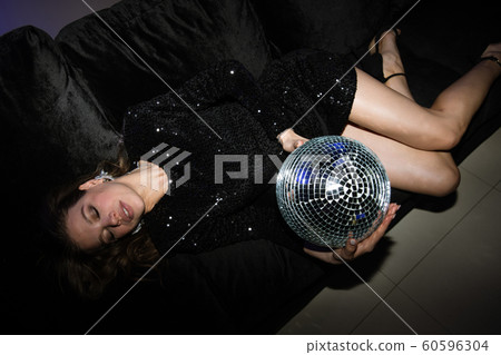 Restful young woman in black glittering dress holding disco ball 60596304