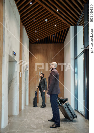 Two traveling businessmen with suitcases waiting for elevator in hotel 60596439