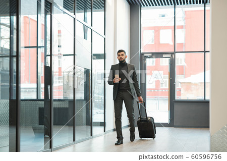 Young elegant businessman with smartphone pulling suitcase with luggage 60596756