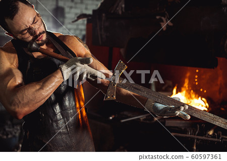 portrait of blacksmith studying handmade metal in workshop 60597361