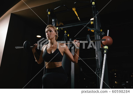Front view of confident young blonde woman doing weight lifting workout Attractive young woman lifting weight looking forward Strong trained body shape arms chest legs. 60598284